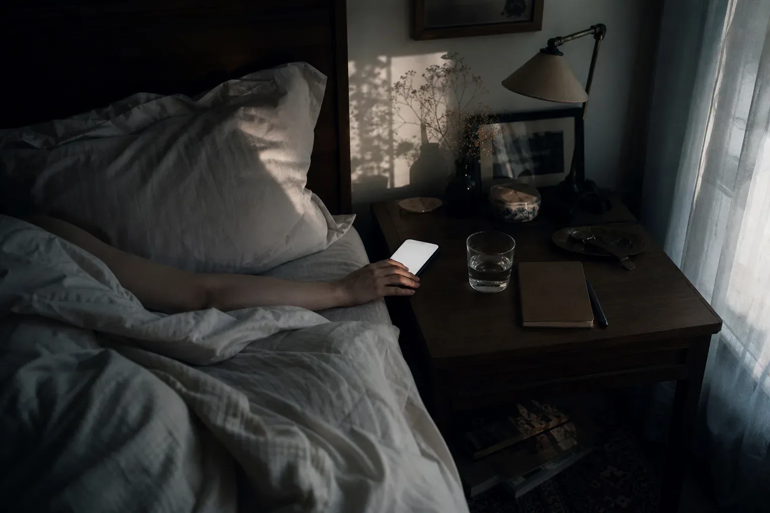 Person holding glowing phone beside an unmade bed